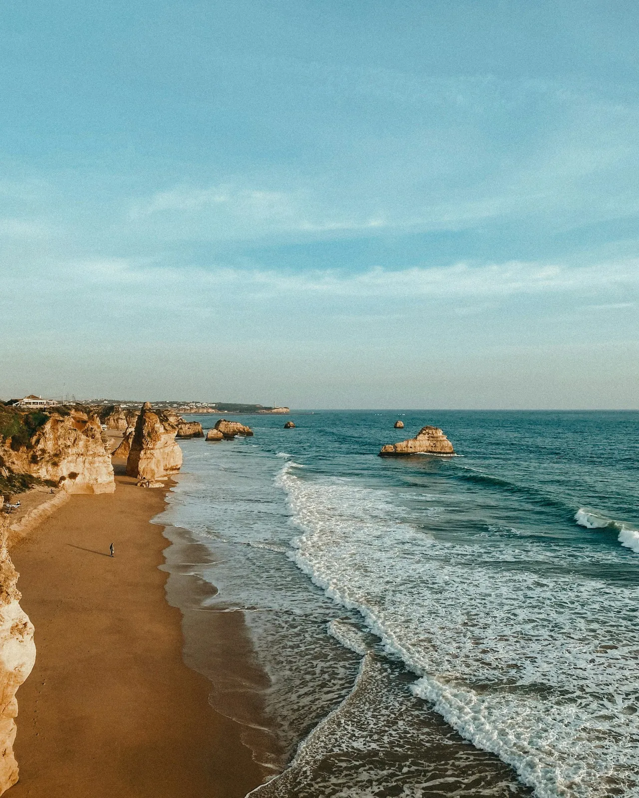 Plage de l'Algarve avec falaises ocre et eaux turquoise de l'Atlantique au coucher du soleil